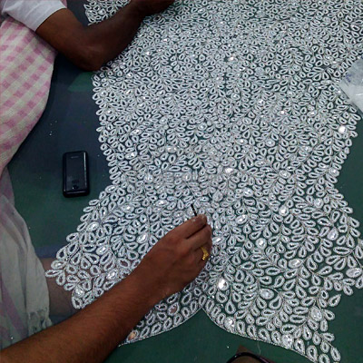 Artisan creating dense white hand embroidery on an adda frame